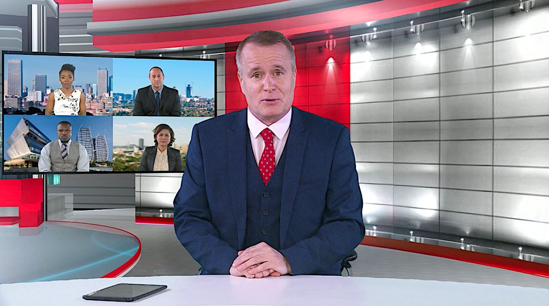 A presenter in a news-style studio with video call panels on a screen