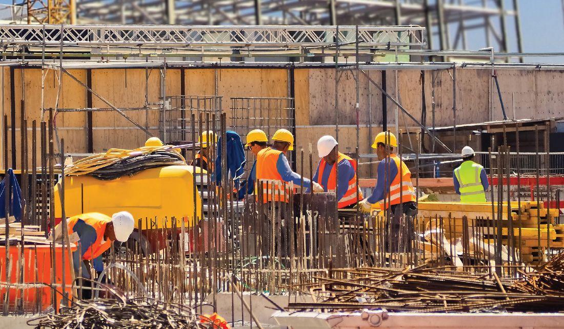 Workers on a large construction site with steel rebar and scaffolding