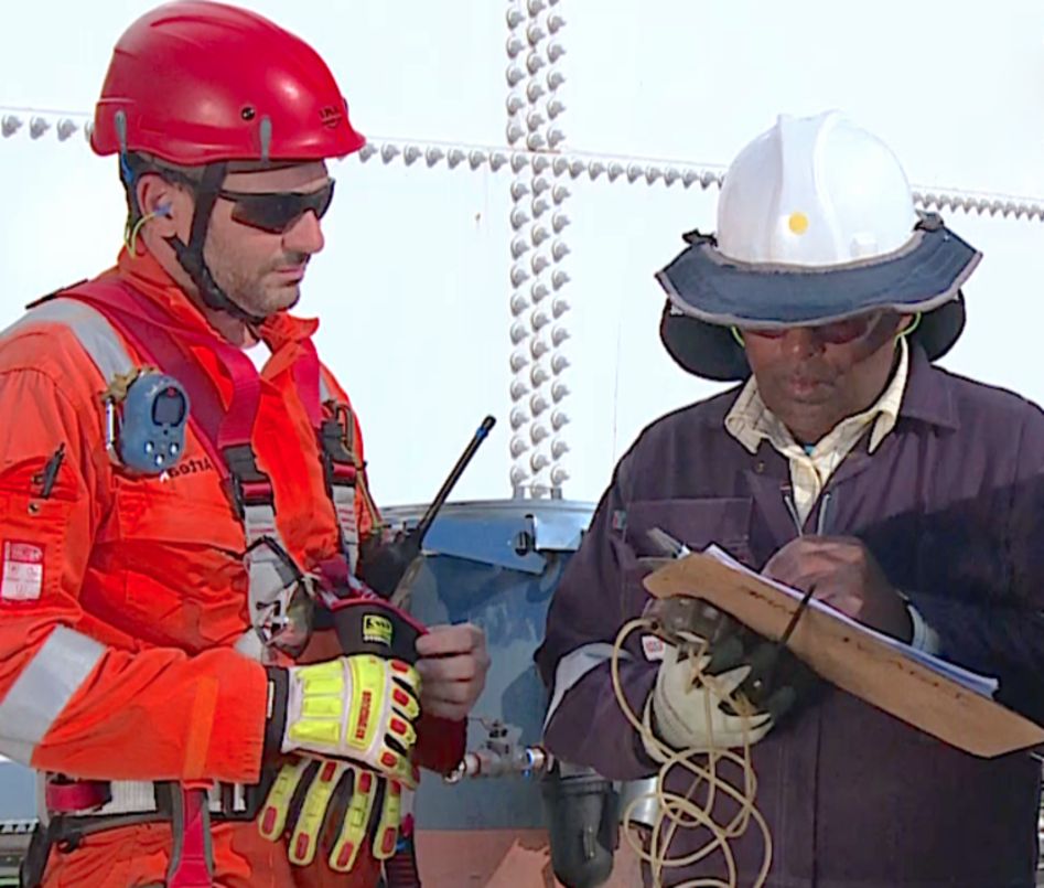Two workers in safety gear on a construction site, one writing on a clipboard
