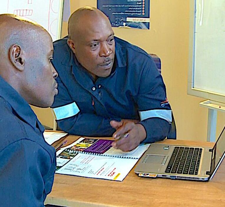 Two men reviewing material on a laptop during a training session